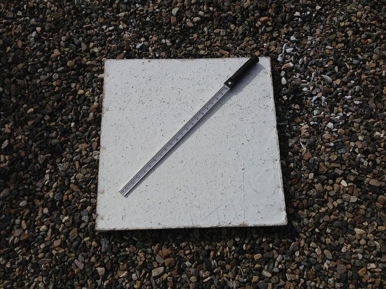 square white board with measuring stick lying across it on the ground